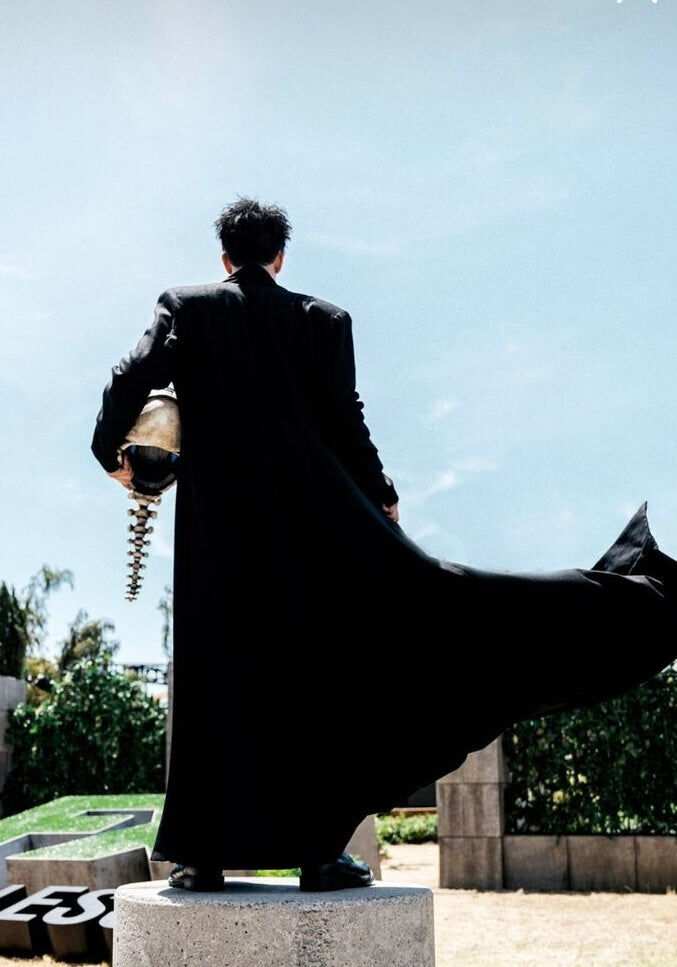 A full length black wool trench coat with the skirt caught mid air against an open sky