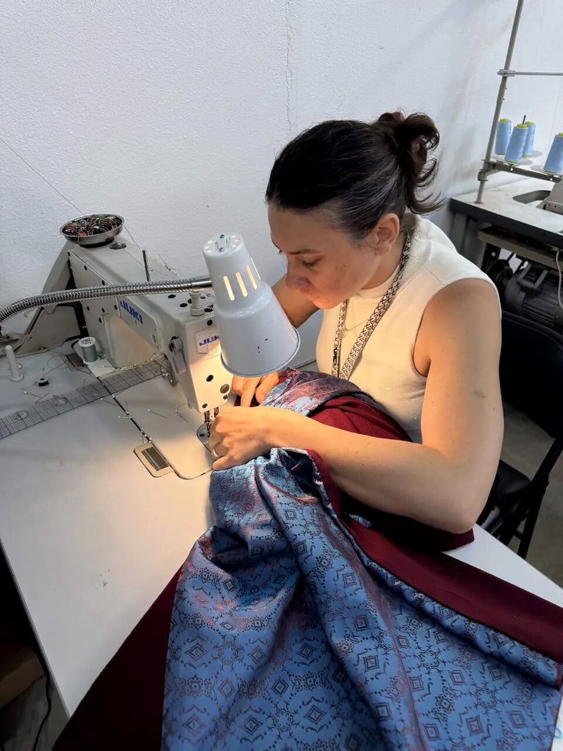 Guiding a burgundy garment with blue paisley lining through an industrial machine